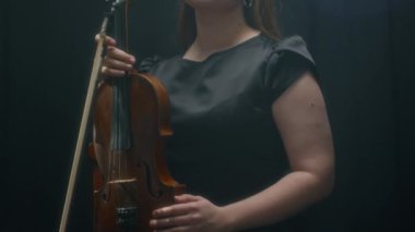 Genç beyaz kadın müzisyenin kemancı portresini yukarı kaldır ve siyah arka planda dikilirken kameraya güven içinde bak.