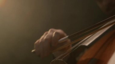 Koyu arkaplanda yaylı bir enstrüman çalan çellistin tanınmaz hale gelmiş zarif elinin yakın çekimi