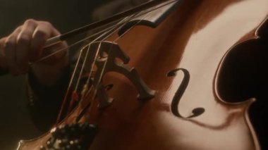 Siyah arka planda çello çalan, takım elbiseli tanınmayan bir erkek müzisyenin görüntüsü.