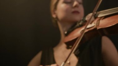 Karanlık sahnede ifadeyle oynayan zarif beyaz kadın kemancının orta boy yakın çekimi.