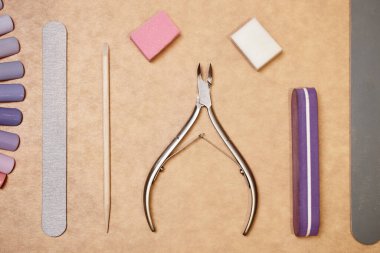 Bej arka planda tırnak bakımı için temel araçların düz çekim. Tırnak törpüleri, tampon bloklar, turuncu çubuk ve tırnak uçlarında manikür, el bakımı kavramı.