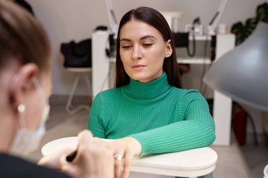 Zümrüt yeşili kazaklı genç esmerin portresi. Güzellik salonunda manikür yaptırıyor.