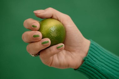 Zümrüt zümrüt zemin üzerinde yeşil çizgili, taze limonlu, kopyalama alanı olan şık, nötr kadın tırnaklarının stüdyo çekimi.