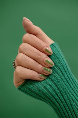 Zümrüt zemin üzerinde minimalist yeşil çizgi desenli kadın badem şekilli tırnaklarının dikey stüdyo çekimi, kopyalama alanı
