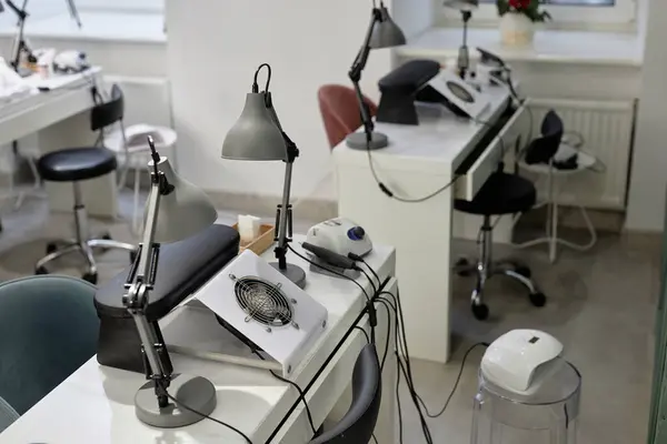 stock image Shot of manicurist workplace equipped with nail tech desks with dust collectors and table lamps. White clean interior of empty beauty salon