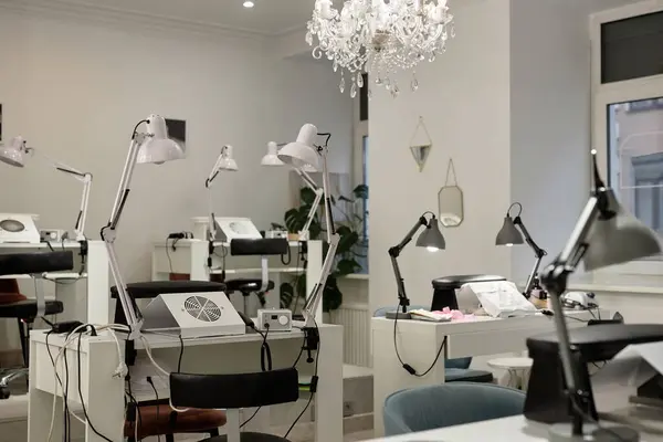 stock image Shot of nail salon interior in modern minimalistic style with chandelier ceiling light, manicurists desks and lamps, copy space