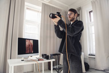 Beyaz stüdyo içinde profesyonel fotoğraf çekimi sırasında çekilen düşük açılı erkek fotoğrafçı portresi, boşluğu kopyala 