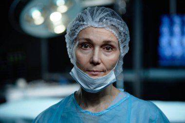 Kadın cerrah kıdemli kadın portresi. Ameliyathanede maske takıp kameraya bakıyor.