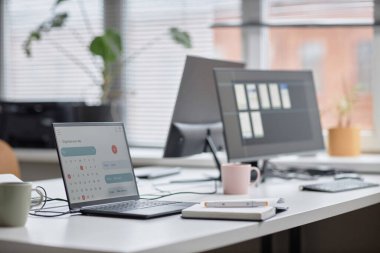 Ofis iş yeri tablosunun pastel renklerinde çekilen yan görüntü, dizüstü bilgisayarın takvim sayfası, defter ve bilgisayar monitörleri arka planda, ekrana odaklan, alanı kopyala