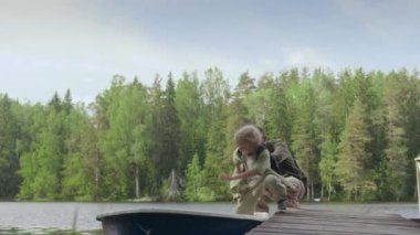 9 yaşındaki beyaz bir çocuğun yaz mevsiminde babamla nehirde balık tutmaya giderken tahta iskeleden tekneye binerken çekilmiş uzay fotoğrafını çek.