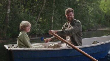 Beyaz bir baba ve oğul yazın nehirde kürek çekerken balıkçı teknesinde oturuyorlar.