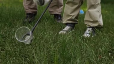 Beyaz tenli baba ve oğulun yaz mevsiminde parkta yeşil çimlerden plastik çöp toplaması.