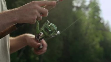 Doğada balık tutarken oltasının üzerinde dönen bir balıkçının tanınamaz haldeki elleri.