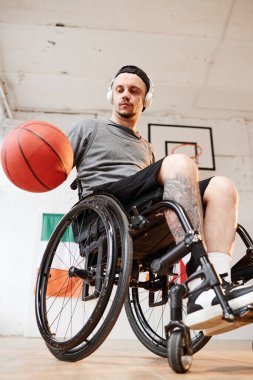 Kapalı alanda basketbol oynarken engelli top süren genç sporcunun dikey düşük açılı çekimi.
