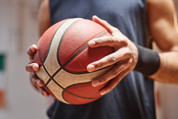 Крупный план неузнаваемого молодого чернокожего человека, держащего баскетбольный мяч в руках с драматическим светом копирования пространства