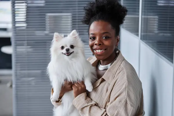 stock image Medium close up of African American female pet owner with cute white pomeranian on hands smiling and looking at camera while waiting for appointment in vet clinic, copy space