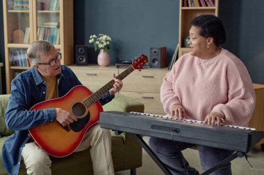 Huzurevinde yaratıcı hobilerin keyfini çıkarırken müzik çalan ve birlikte şarkı söyleyen yaşlı insanların ön manzara portresi.