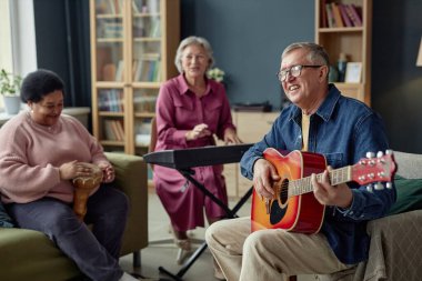 Bir grup neşeli son sınıf öğrencisi birlikte müzik yapıyor. Emeklilik evinde yetenek gösterisinin keyfini çıkarıyor. Gülümseyen son sınıf öğrencisinin gitar kopyalama alanına odaklanıyor.