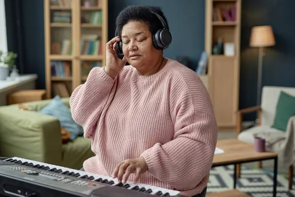 stock image Portrait of inspired senior woman playing piano at home and wearing headphones while composing music