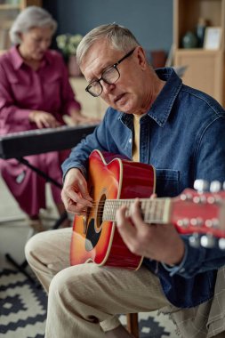 Yaşlılar yurdunda gitar çalan ve şarkı söyleyen beyaz bir adamın dikey portresi.
