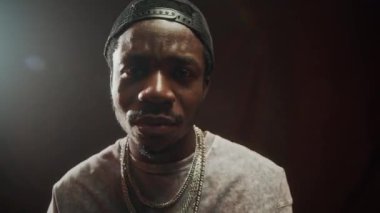 Siyah stüdyonun arka planında dikilirken kameraya güvenle rap yapan havalı siyahi adamın göğsü.