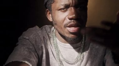 Göğsünde siyah arka planda projektör ışığı olan, gümüş zincirli kolyeli havalı Afrikalı Amerikalı adam var.