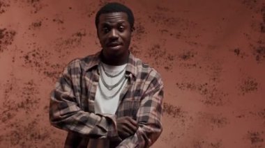 Artistik siyah erkek manken, ekose gömleğin altına beyaz tişört giyip boynundaki gümüş zincirlerle kameraya poz verirken aynı zamanda kırmızı arka planda yaratıcı stüdyo fotoğraflarına sahip.