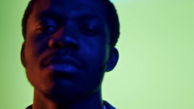 Kendine güvenen genç siyahi adamın yakın plan portresi canlı neon arka planda duran kameraya bakıyor açık yeşilden parlak kırmızıya renk değiştiriyor.