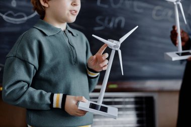 İlkokul erkek öğrencisinin küçük güneş enerjili rüzgar türbini tutarken sınıfa yeşil enerjiden bahsederken çekilmiş görüntüsü.