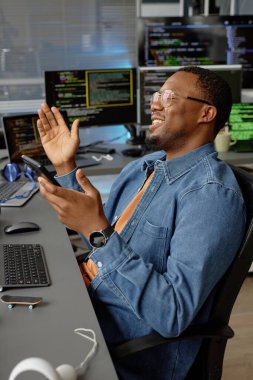 Afrika kökenli Amerikalı mutlu erkek yazılım geliştiricisinin ofis başarısını kutlarken birden fazla ekranla birlikte dikey çekimi, boşluğu kopyala