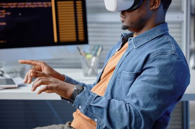 Ofis işyerindeki VR sistemlerini kullanarak kulaklık takan konsantre erkek Afro-Amerikan yazılım mühendisinin yan görüntüsü.