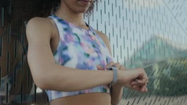 Kıvırcık saçlı, kablosuz kulaklık takan, fitness takip cihazı takan ve yaz günü dışarıda egzersiz yaparken şehir caddesinde koşan bir kızın yavaş çekim görüntüsü.