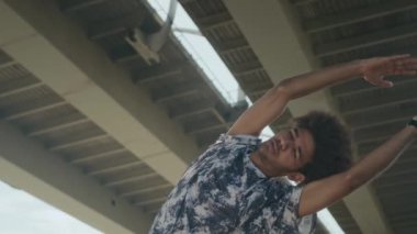 Kıvırcık saçlı, kenar kıvrımlı ve kalça çevirme egzersizi yapan genç bir adamın açık hava eğitiminden önce şehir merkezinde ısınma hareketleri.