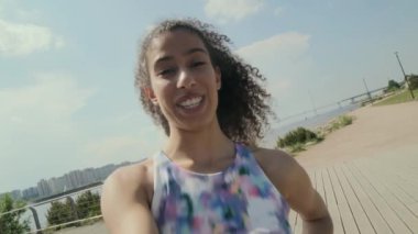 Spor giyim sektöründe genç, neşeli atletik bir kız. Kaslarını gösteriyor, gülümsüyor ve kamerada konuşuyor. Şehir sokaklarında fitness vlog 'unu çekerken.