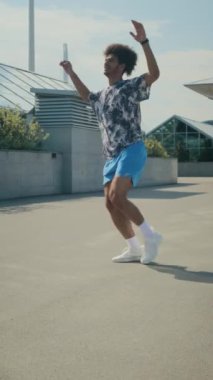 Ayaklarıyla hoplayan, el çırpan, ayak bileklerini ısıtan ve şehir dışında egzersiz yapan genç bir sporcunun dikey çekimi.