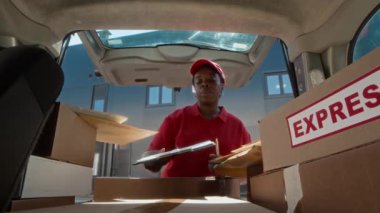 Kutu ve paketlerle dolu bagajı boşaltan klasörde teslimat formu olan kadın siyah kuryenin düşük açılı görüntüsü