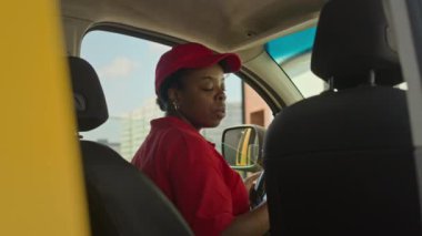 Müşterilere teslimat yaparken Afrika kökenli Amerikalı kadın kuryenin arabanın arka koltuğundan paket alırken elde çekilmiş bir fotoğrafı.