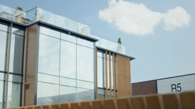 Tabelalı modern depo cephesi, büyük cam pencereler, tahta kirişler ve temiz mavi gökyüzüne karşı cam korkuluklu çatı katı.