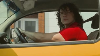 Kırmızı üniformalı, sarı minibüslü, ciddi, beyaz erkek teslimat servisi çalışanının yan görüntüsü.