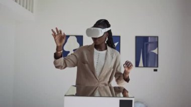 Görünmez eşyalara dokunan ve sanal gerçeklikteki sergiyi keşfederken gülümseyen Afro-Amerikan kadının görüntüsünü büyüt.