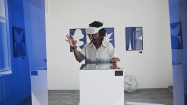 Çağdaş sanat galerisinde dikilirken ve artırılmış gerçeklikte sergi keşfederken VR kulaklık takmış genç siyahi bir adamın görüntüsü.
