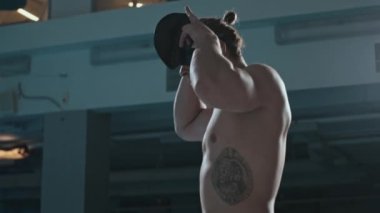 Beyaz erkek yüzücüyü yavaş çekimde yukarı kaldır. Kaburgasında siyah dövme var. Kapalı havuzda yarışa başlamadan önce yüzme şapkası takıyor.