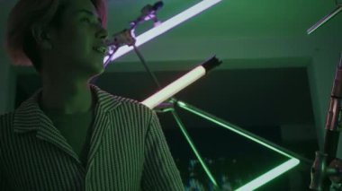 Asyalı Gen Z adamı karanlık odada ışık kurulumundan geçiyor ve galerideki kavramsal sanat sergisini ziyaret ederken onu ilgiyle izliyor.