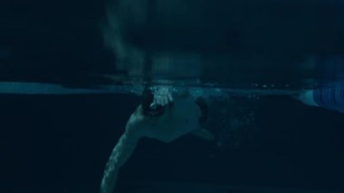 Mavi havuz suyunda hareket halinde olan kararlı beyaz erkek yüzücünün sualtı çekimi.