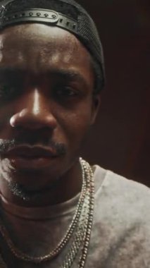 Havalı siyahi adamın dikey göğsü siyah stüdyonun arka planında dikilirken kameraya güvenle rap yapıyor.