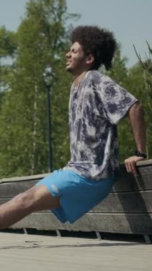 Aktif giyimli genç ve güçlü bir adamın sokak sporu sırasında bankta dalış yaptığı dikey çekim.