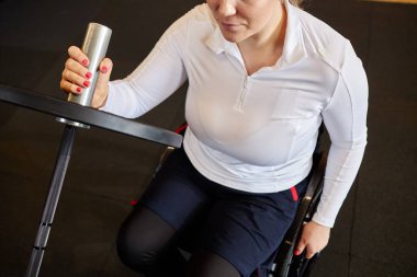 Spor salonunda tekerlekli sandalye kullanan ve halter fotokopi yeriyle egzersiz yapan tanınmamış bir kadının üst görüntüsü.