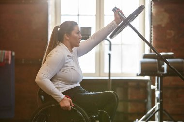 Özürlü yetişkin kadın portresi bulanık spor salonunda halterle ağırlık çalışmasının keyfini çıkarıyor.