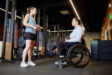 Beden eğitimi dersinde engelli bir kadına yardımcı olan bayan fitness eğitmeninin tam boy yan görüntüsü.