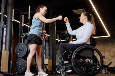 Spor salonundaki başarılı eğitimden sonra gülümseyen engelli bir kadınla kadın spor salonu antrenörünün tam boy yan görüntüsü.